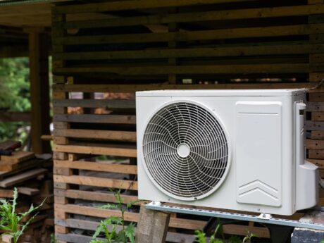 New modern HVAC air conditioning external compressor unit near wall of wooden log residential country cottage