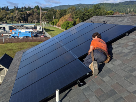 Six Rivers Solar staff person atop roof tinkering with solar panels